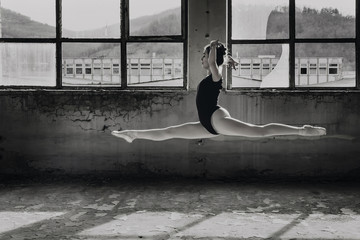 Black and white photo of ballerina doing split leap, jump in an old building