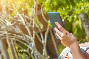 Girl hand holds an aquamarine ebook. Against the backdrop of green trees in summer.