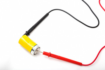Multimeter wires and yellow battery. Checking battery voltage. Red to plus. Close up, isolated on white background