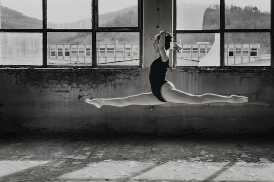 Black and white photo of ballerina doing split leap, jump in an old building
