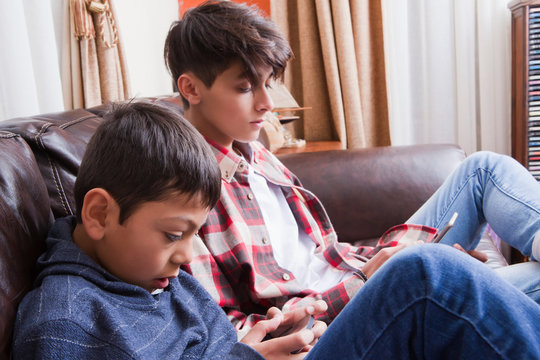 Brothers using smart phones on sofa