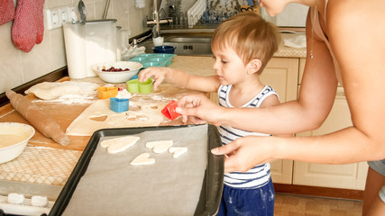 Closeup portrait of young mother with toddler boy holding baking pan and making cookies on kitchen