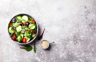 Vegetable salad in a glass bowl with greens, olive oil and sesame  on a gray background.Vegetarian. Concept for a tasty and healthy meal. Copy space for Text.Top view.