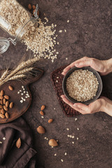 Woman hands hold full bowl of oatmeal flakes. Cooking oats porridge with almond nuts on dark background. Top view.