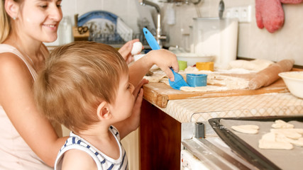 Portrait of cute little boy with young mother baking cookies on baking pan at kitchen