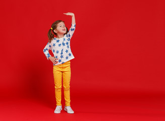 concept of development and growth,   kid girl measuring height on  red colored background.
