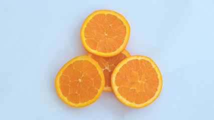 Four orange slices lay on a white background with one slice in the middle laying under the remaining three resting on top of it creating beautiful food art.