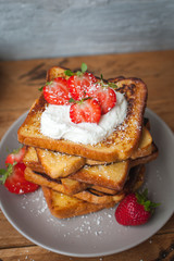 Close-up of french toast with fresh strawberries, coconut shreds and honey, on wooden background