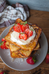 Close-up of french toast with fresh strawberries, coconut shreds and honey, on wooden background, top view