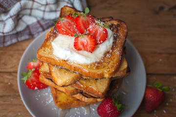 Close-up of french toast with fresh strawberries, coconut shreds and honey, on wooden background