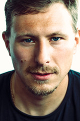 Obraz premium Colored closeup portrait of caucasian man with blue eyes, mustache, little beard and gold chain in black t-shirt 