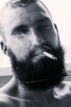 Monochrome closeup portrait of man with mustache and beard smoking cigarette 