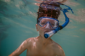 Naklejka premium Child snorkeling. Young boy wearing diving mask and snorkel swimming under water.