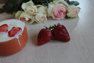 Bouquet of beautiful red roses and strawberries with cream lie on the bright wooden background.