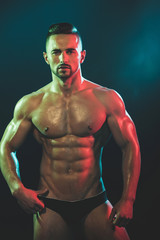 Fototapeta na wymiar Muscular naked man touching his black underwear. Sporty shape of young man. Portrait of tanned young bearded bodybuilder with perfect muscular body. Advertising concept of strip club. Sport concept.