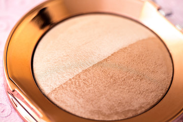 Powder on a pink background, macro image of cosmetics, two-tone bronzer and highlighter