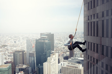 Businessman climbs a building with a rope. Concept of determination