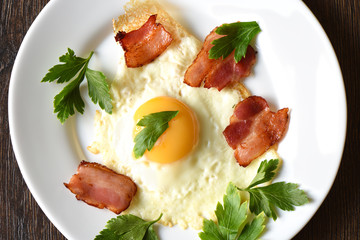 Fried eggs with bacon and parsley on a white plate.