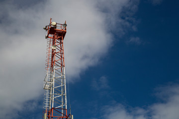 Cell phone antenna tower in a blue sky with clouds.