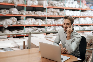 Warehouse manager sitting at his desk talking on a cellphone