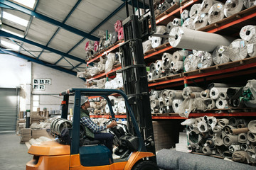 Worker using a forklift to remove stock from warehouse shelves