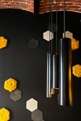 Black wall with decorative orange and yellow honey cell of moss and loft creative lamp. In interior of cafe . Loft space design creative minimalistic cafe interior, simplicity and geometry concept, 