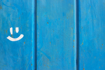 Old blue painted corrugated metal fence with stains, scratches, traces of dirt and rust and drawn smile.