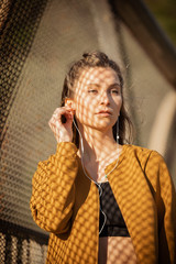 Young woman listening to music while standing by fence outdoors