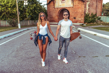 Young couple man woman walking summer city, skate longboard. Youth fashion style, modern leisure trend, tanned sports figure. Emotions of happiness, pleasure, relaxation, having fun weekend.