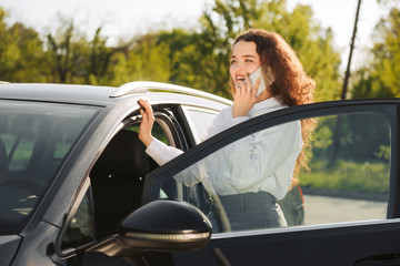 Business woman talking on the phone in the parking lot. Stylish young woman standing near the car
