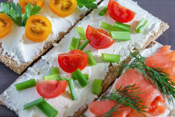 Crispbread with soft cheese, trout, tomatoes, dill and green onions, close-up. Light summer snack. Bright picture.