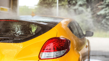 Roof and side of yellow car washed in self serve carwash, water spraying from the hose, view from...