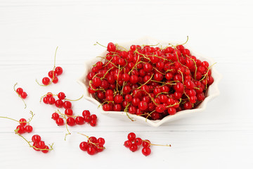 Red currant are located in a plate on a white background
