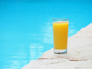 a glass of orange juice near the swimming pool.