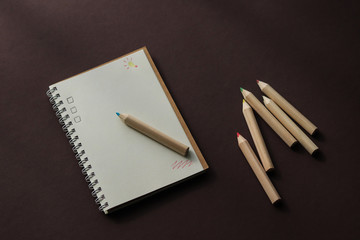 school notebook on a brown background, a spiral notebook and colored pencils on the table