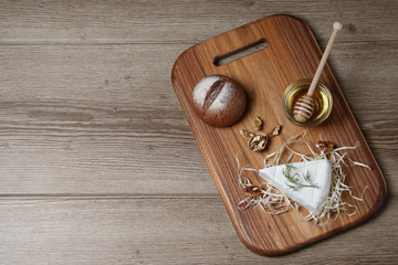 Top view of brie cheese with nuts, bun and honey on a wooden board and dark background. The concept of still life. Space for text