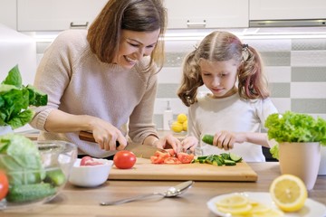Cooking healthy home meal by family. Mother and daughter cut vegetables at home in the kitchen for salad