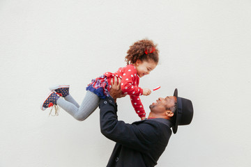 strong dad lifting up his sweet little kid. African american family having a bonding moment on a light background