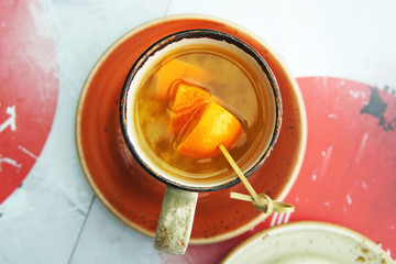 A cup of citrus tea with mango and orange slices on an orange saucer in a Japanese cafe. View from above.