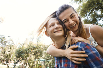 Portrait of young couple having fun and laughing in park. Boyfriend carrying his girlfriend on back.