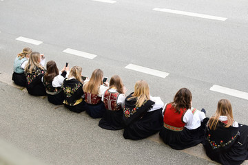 The girls are sitting on the side of the road with mobile phones. A group of people in national...