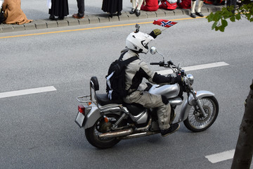 Motorcyclist with an action camera on the helmet and the flag of Norway rides on the highway.