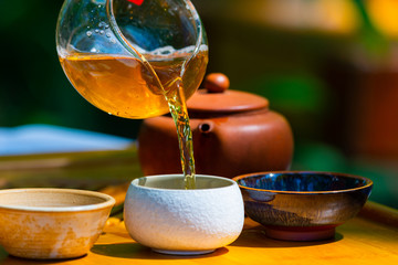 On the table on a wooden tray a teapot with tea, teapot, cups. Man, hands pouring tea