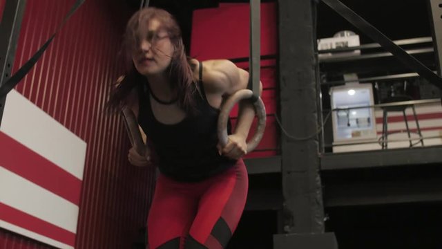 Woman in red sport pants is doing climb up on the gymnastic rings