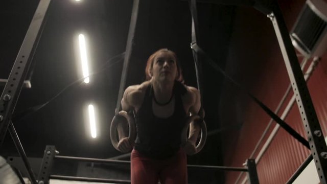 Athletic girl is doing climb up on the gymnastic rings in sport gym