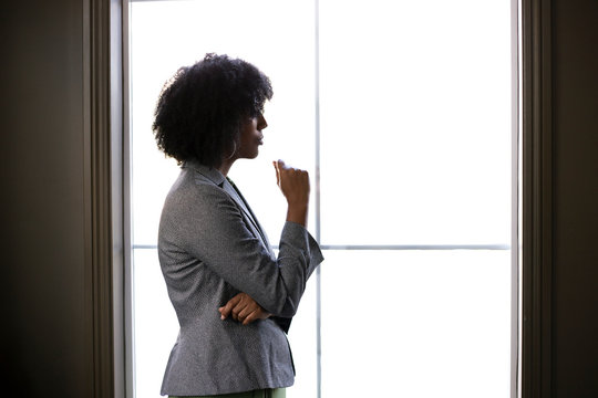 Silhouette of a stressed out black African American businesswoman looking worried and thinking about problems and failure by the office window.  She looks depressed or upset about debt or bankruptcy.
