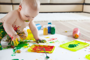 Baby child draws with colored paints hands, dirty feet. White list.