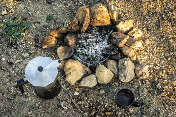 Preparing coffee using a bonfire during a camp in the forest. Bonfire with rocks, coffee maker moka and cup. Preparation of coffee during a trip.