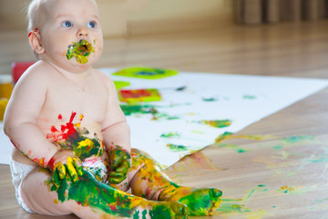 Baby child draws with colored paints hands, dirty feet. White list.