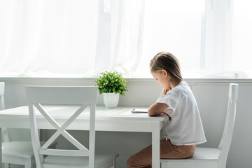 cute kid sitting and writing in notebook at home